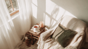 an organized cozy corner in an apartment with a chair, sidetable with tea and candle near a sunny window